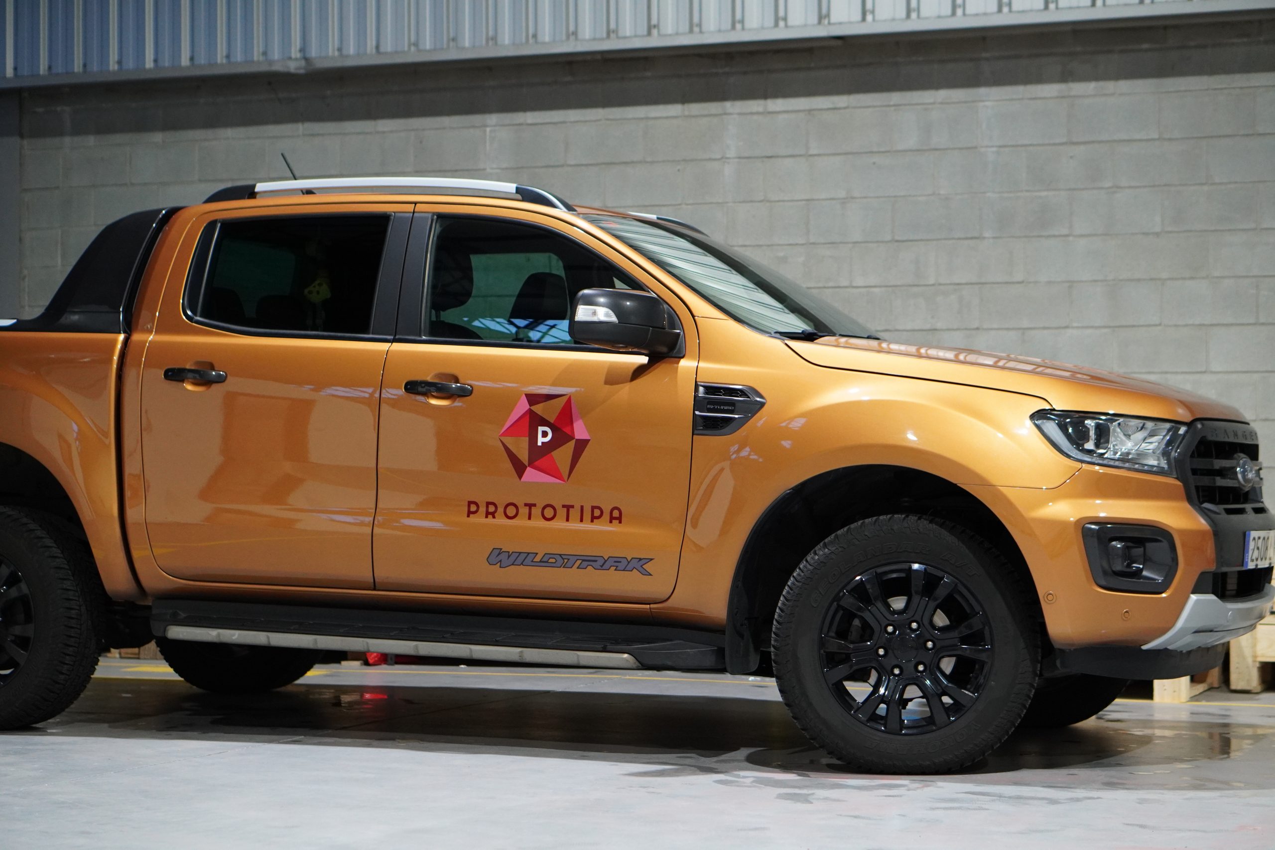 Pick-up naranja con el logotipo de Prototipa en la puerta, dentro de la nave del taller